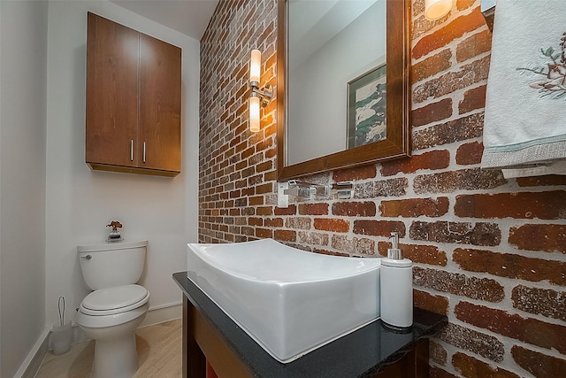 bathroom featuring toilet, vanity, and brick wall