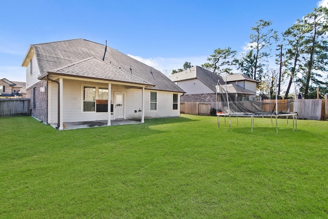 back of house featuring a trampoline, a patio area, and a lawn