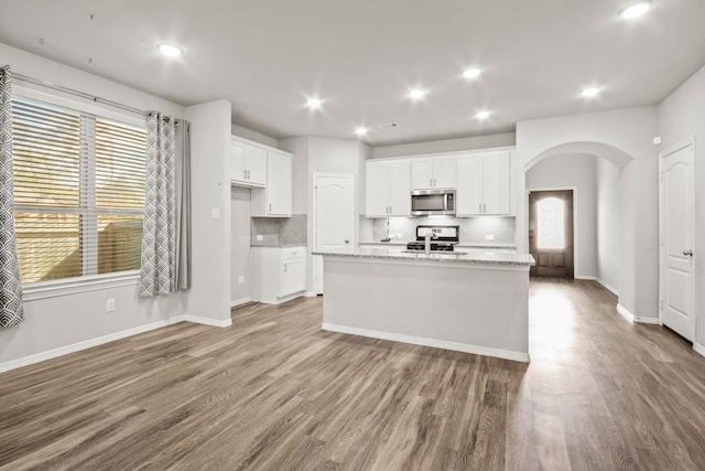 kitchen featuring white cabinets, tasteful backsplash, stainless steel appliances, and an island with sink