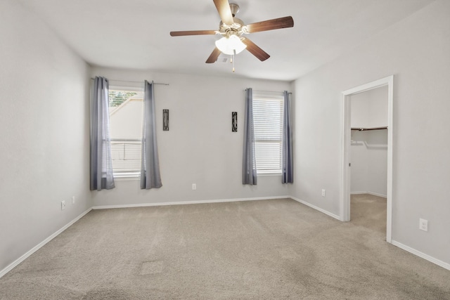 unfurnished bedroom featuring light carpet, a walk in closet, multiple windows, and ceiling fan