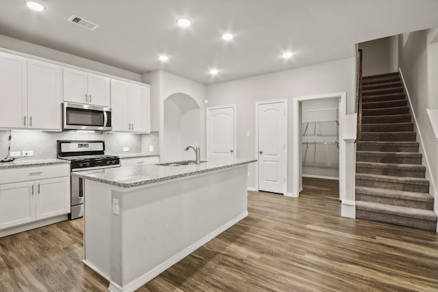 kitchen with white cabinetry, sink, stainless steel appliances, backsplash, and a center island with sink