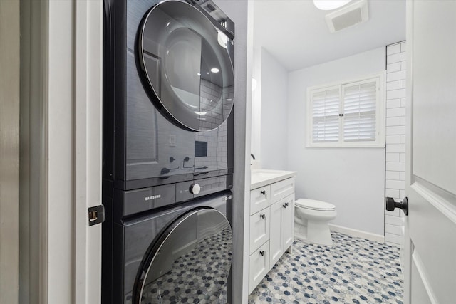 bathroom featuring toilet, vanity, visible vents, baseboards, and stacked washing maching and dryer