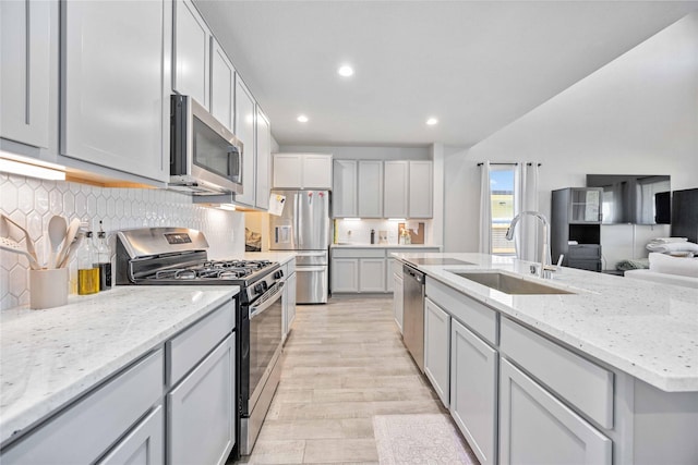 kitchen with sink, gray cabinets, backsplash, stainless steel appliances, and light stone countertops