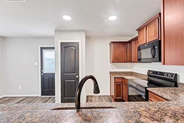 kitchen featuring sink, dark wood-type flooring, dark stone countertops, and black appliances