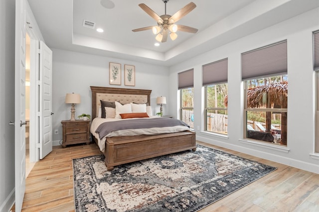 bedroom featuring light wood-type flooring, a raised ceiling, and ceiling fan