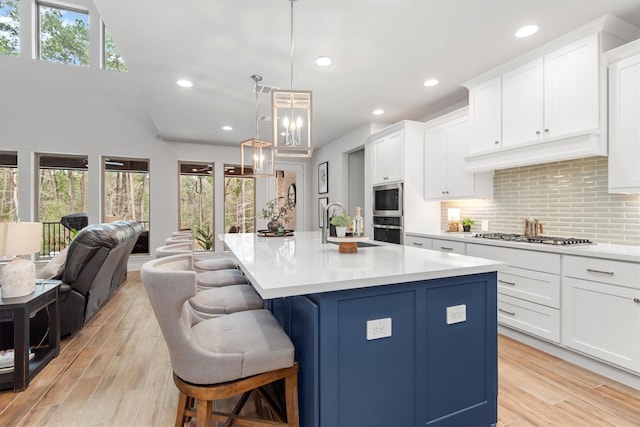 kitchen with backsplash, stainless steel appliances, pendant lighting, white cabinetry, and an island with sink