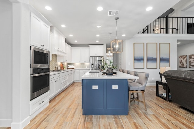 kitchen with decorative backsplash, stainless steel appliances, a kitchen island with sink, pendant lighting, and white cabinets