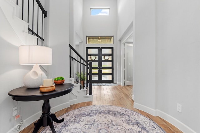 entryway featuring light wood-type flooring, a towering ceiling, and french doors