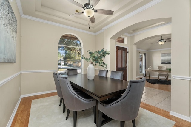 dining space with arched walkways, crown molding, light wood-type flooring, and a tray ceiling