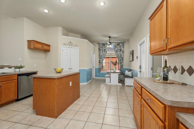 kitchen with light tile patterned floors, a kitchen island, stainless steel dishwasher, and brown cabinetry