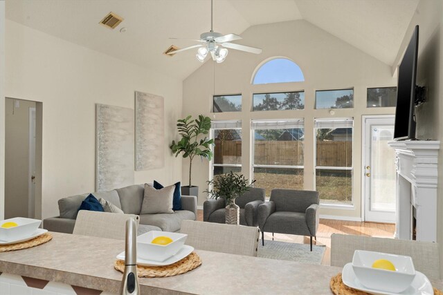 living area with visible vents, a healthy amount of sunlight, high vaulted ceiling, and wood finished floors