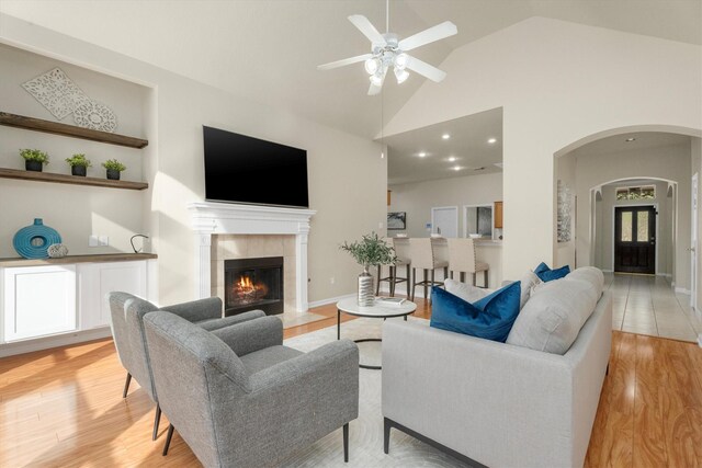 living room featuring light wood finished floors, a fireplace, high vaulted ceiling, and arched walkways