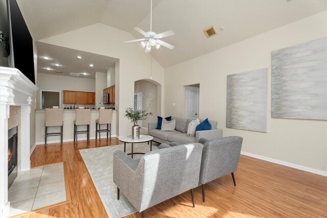 living room with visible vents, light wood finished floors, high vaulted ceiling, a fireplace with flush hearth, and arched walkways