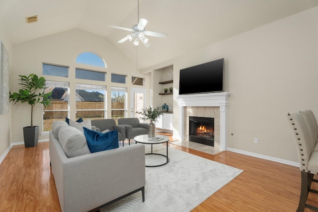 living room featuring built in features, baseboards, a tiled fireplace, visible vents, and wood finished floors