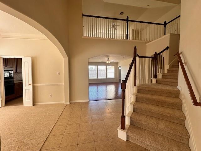 stairs featuring tile patterned floors, ceiling fan, and a high ceiling