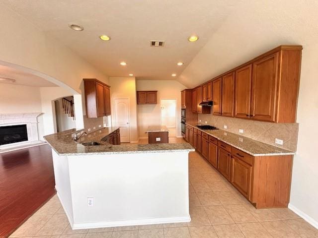 kitchen with lofted ceiling, light tile patterned flooring, light stone countertops, and kitchen peninsula