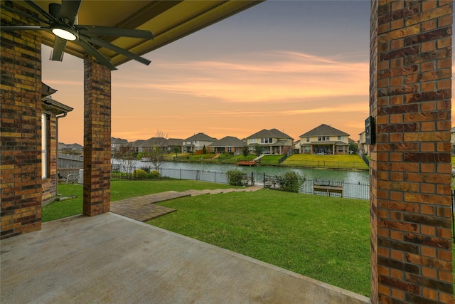 yard at dusk featuring a patio area, ceiling fan, and a water view