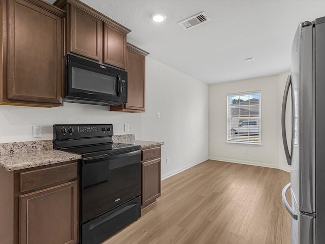 kitchen with dark brown cabinetry, light stone counters, light hardwood / wood-style flooring, and black appliances