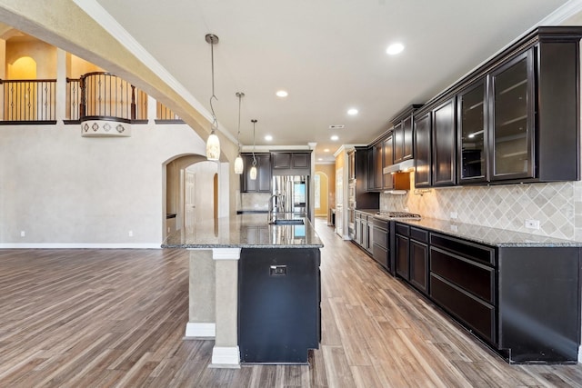 kitchen featuring backsplash, ornamental molding, sink, decorative light fixtures, and an island with sink