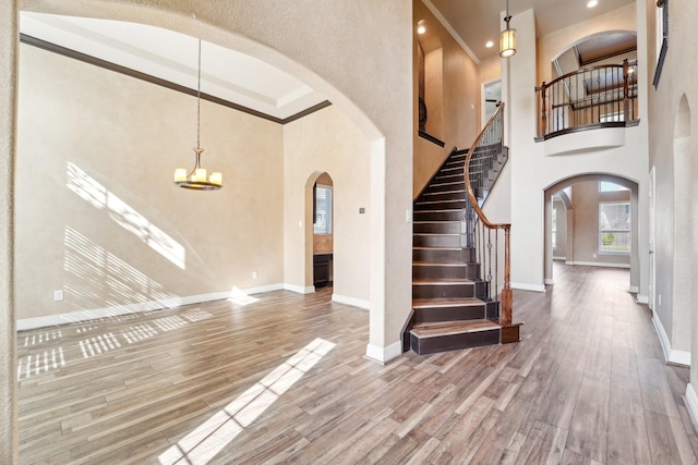 entrance foyer featuring ornamental molding, a towering ceiling, wood-type flooring, and an inviting chandelier