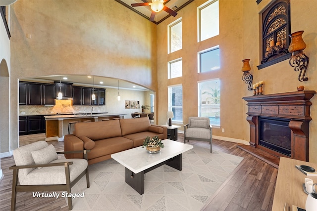 living room with a towering ceiling, light wood-type flooring, and ceiling fan