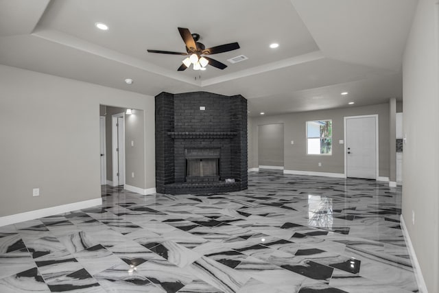 unfurnished living room with a raised ceiling, a brick fireplace, and ceiling fan