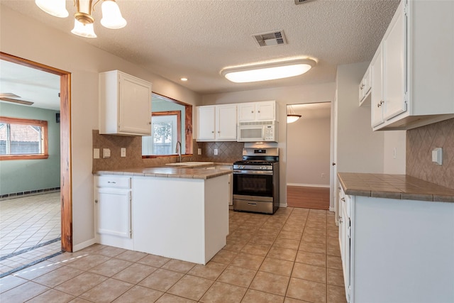 kitchen with white cabinetry, stainless steel gas range, light tile patterned floors, and tile countertops