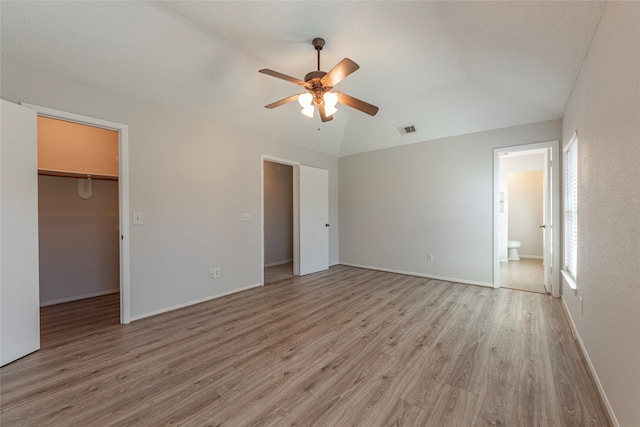 unfurnished bedroom featuring ceiling fan, a walk in closet, connected bathroom, light hardwood / wood-style floors, and a closet