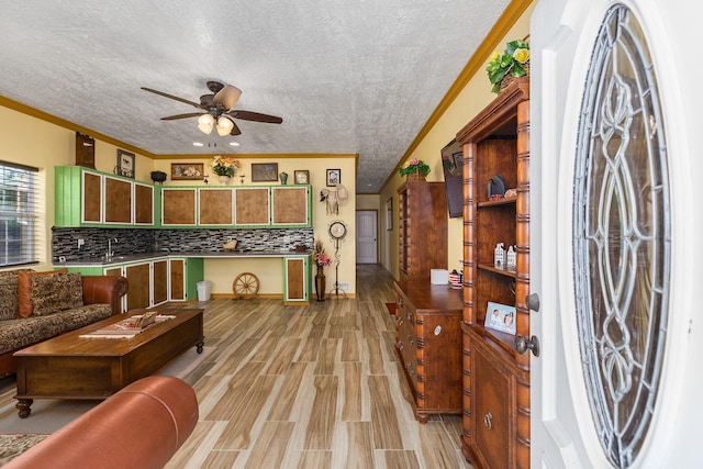 living room featuring a textured ceiling, light wood-type flooring, ceiling fan, and crown molding