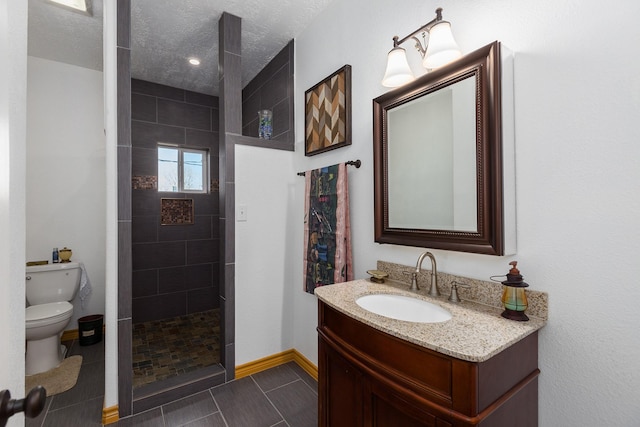 bathroom with a textured ceiling, vanity, toilet, and tiled shower