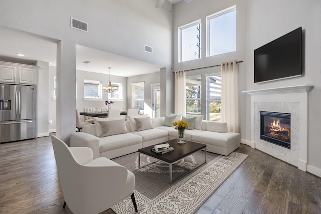 living room with ceiling fan with notable chandelier, a towering ceiling, dark wood-type flooring, and a tile fireplace