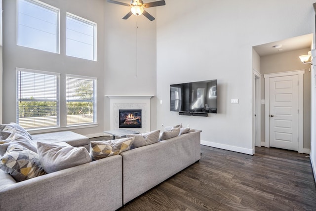 living room featuring a premium fireplace, dark hardwood / wood-style flooring, ceiling fan, and a high ceiling