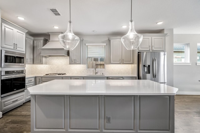 kitchen with appliances with stainless steel finishes, a center island, custom range hood, and pendant lighting