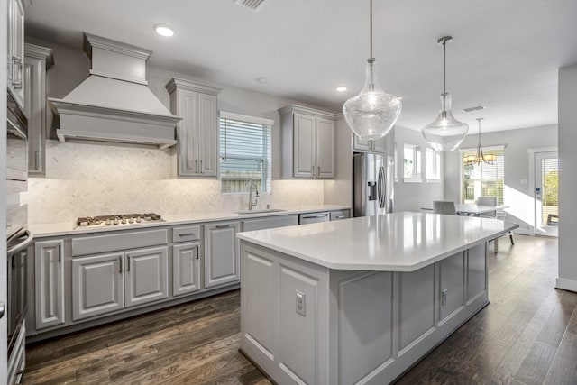 kitchen with custom exhaust hood, sink, decorative light fixtures, a kitchen island, and stainless steel appliances