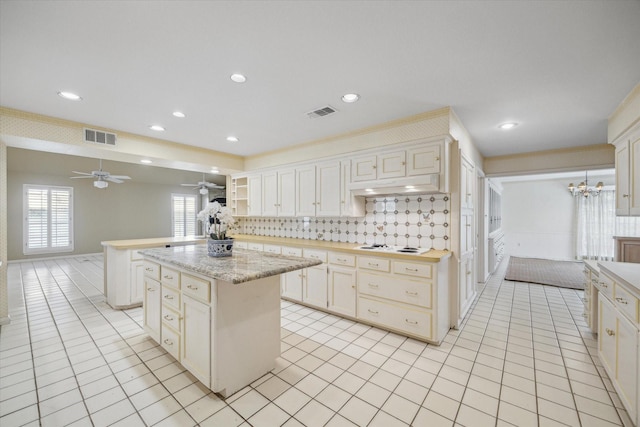 kitchen featuring backsplash, ornamental molding, ceiling fan with notable chandelier, light tile patterned floors, and a center island