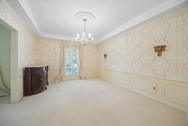 spare room featuring a raised ceiling, a chandelier, and light colored carpet