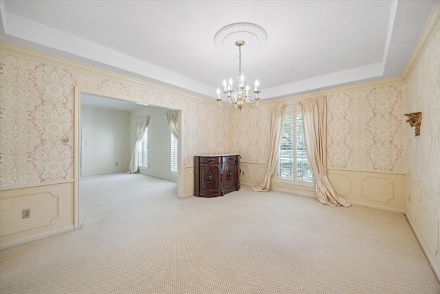 carpeted empty room featuring a raised ceiling, crown molding, and an inviting chandelier