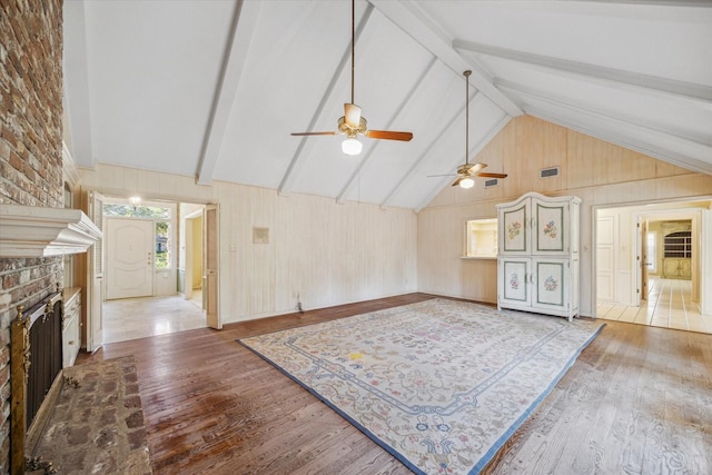 living room with ceiling fan, beamed ceiling, high vaulted ceiling, a fireplace, and hardwood / wood-style flooring