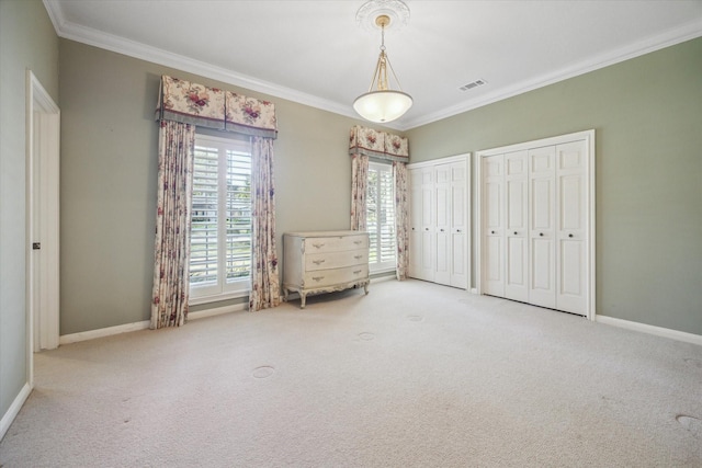 unfurnished bedroom with carpet floors, ornamental molding, and two closets