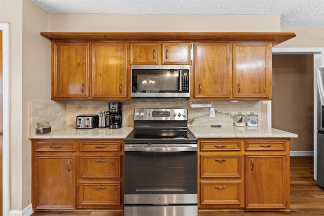 kitchen featuring a textured ceiling, appliances with stainless steel finishes, backsplash, and light stone countertops