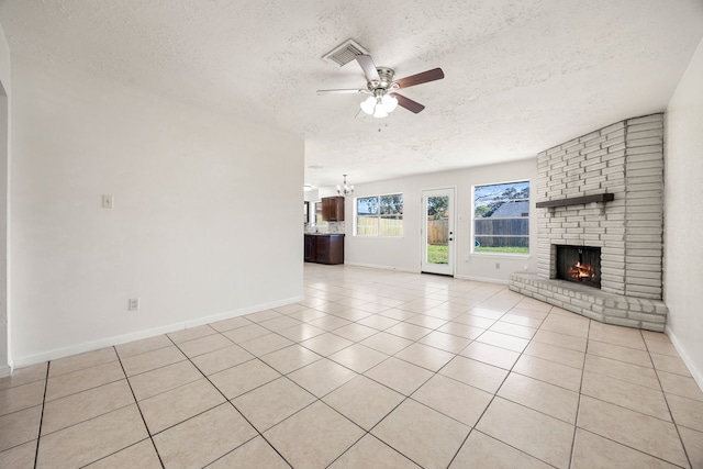 unfurnished living room featuring ceiling fan with notable chandelier, a textured ceiling, and a brick fireplace