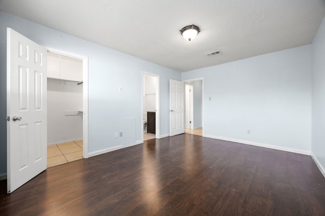 unfurnished bedroom with a walk in closet, ensuite bathroom, a closet, and dark wood-type flooring