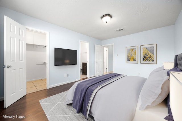 bedroom with ensuite bath, dark hardwood / wood-style floors, a spacious closet, a textured ceiling, and a closet