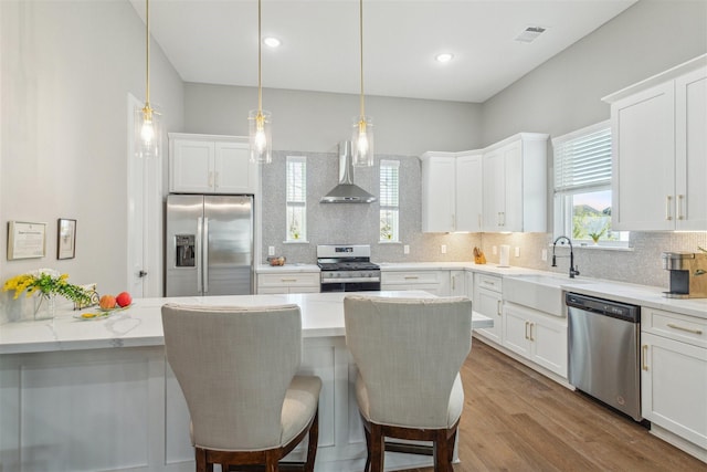 kitchen with visible vents, wall chimney exhaust hood, appliances with stainless steel finishes, a sink, and backsplash