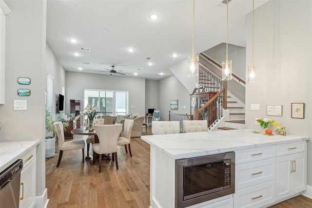 kitchen featuring stainless steel microwave, light wood-style floors, white cabinets, light stone countertops, and dishwasher