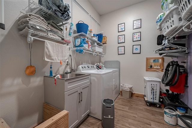 laundry room with washing machine and dryer, light hardwood / wood-style flooring, cabinets, and sink