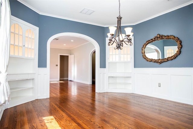 unfurnished dining area featuring built in shelves, crown molding, dark hardwood / wood-style flooring, and an inviting chandelier