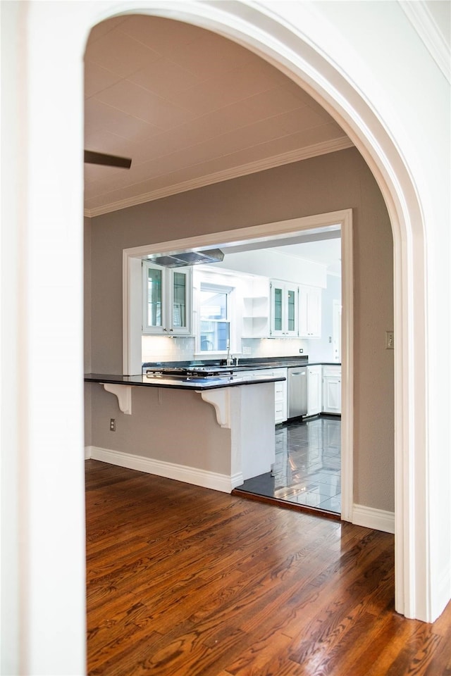 kitchen featuring white cabinetry, dark wood-type flooring, kitchen peninsula, a breakfast bar area, and ornamental molding