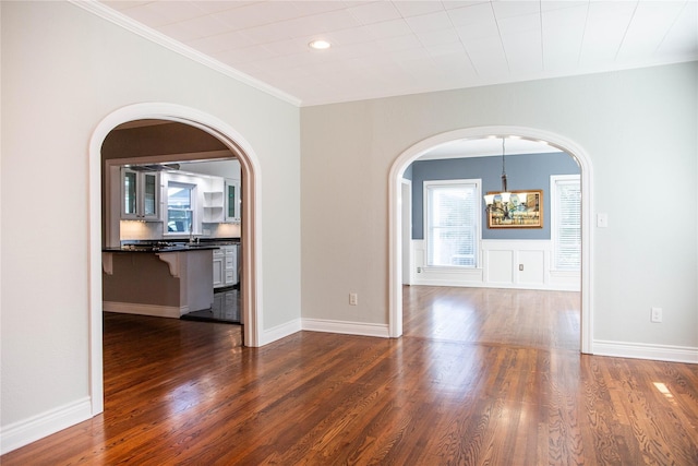 empty room with dark wood-type flooring, crown molding, a notable chandelier, and sink