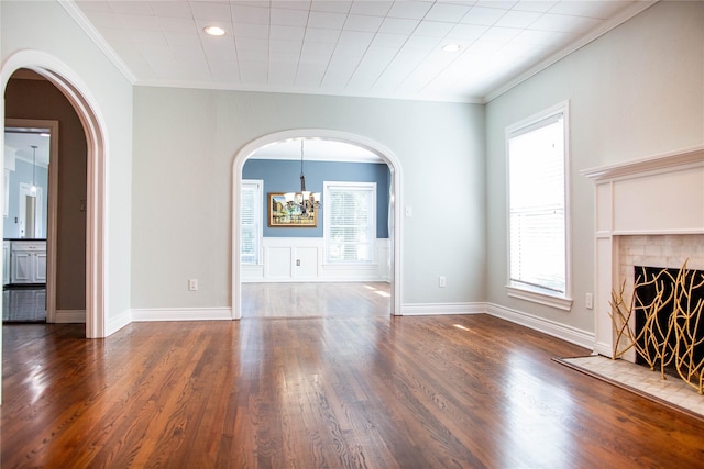 unfurnished living room with a tiled fireplace, dark wood-type flooring, a chandelier, and ornamental molding